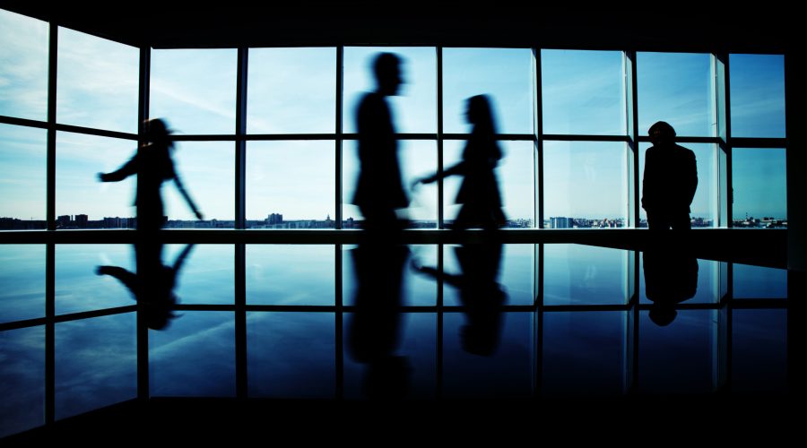 Silhouettes of several office workers walking on background of window