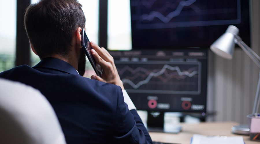 Back view of young business bearded man having a phone call with his CEO. Diagrams on computer monitor.